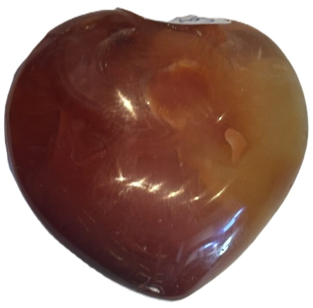 Smooth polished carnelian carved heart palm stone with translucent amber red tones and natural circular orbicular inclusions isolated on a white background